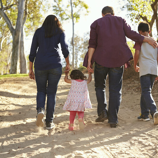 Mixed race family walking on rural path, close up back view